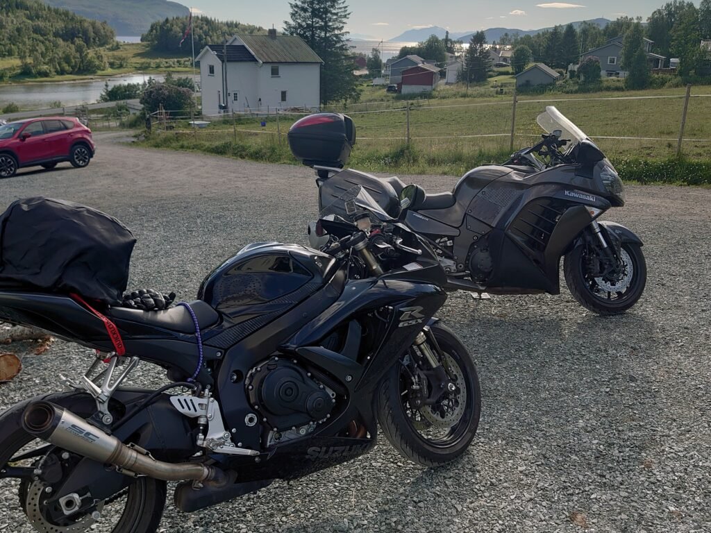 Suzuki ja Kawasaki moottoripyörät parkissa Norjan Sørreisassa, taustalla pihapiiri, talo ja vuonomaisema.